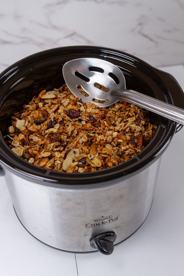 a crock pot full of granola with a metal spoon to the side.