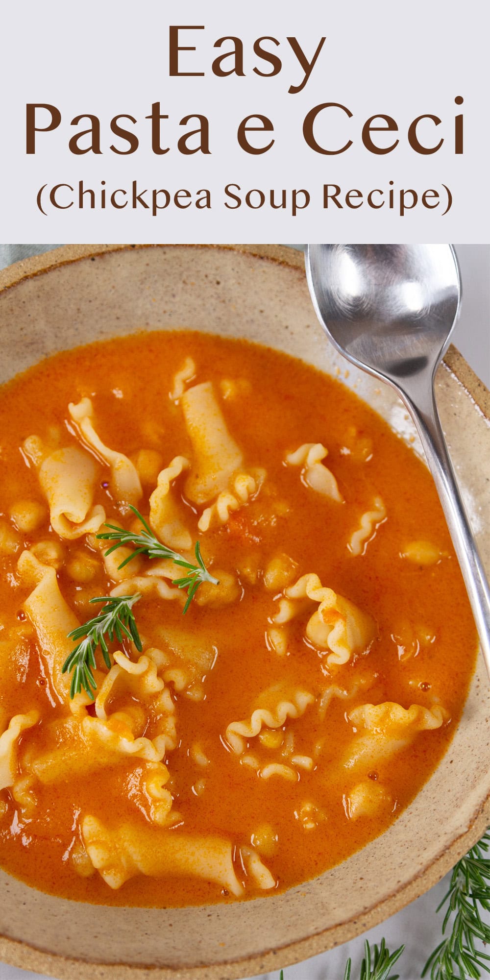 a bowl of tomato noodle soup with a spring of rosemary garnish.