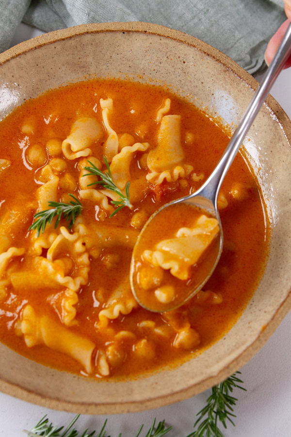 a spoonful of noodle soup above the bowl of soup.