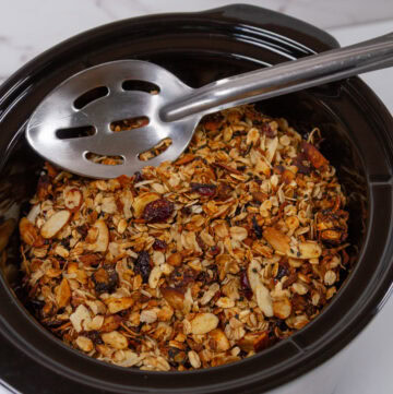 a slow cooker filled with granola and a spoon in the upper area.