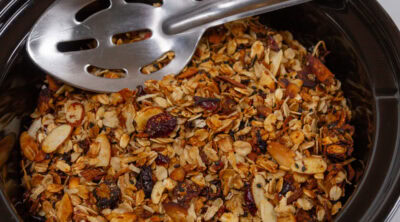 a slow cooker filled with granola and a spoon in the upper area.