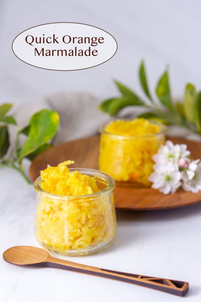 two glass jars with orange marmalade, a wooden plate and spoon, and some flowers.