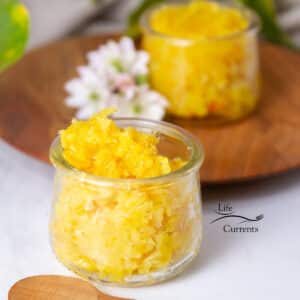 two small glass jars filled with orange marmalade, some flowers around, and a wooden plate in the background.