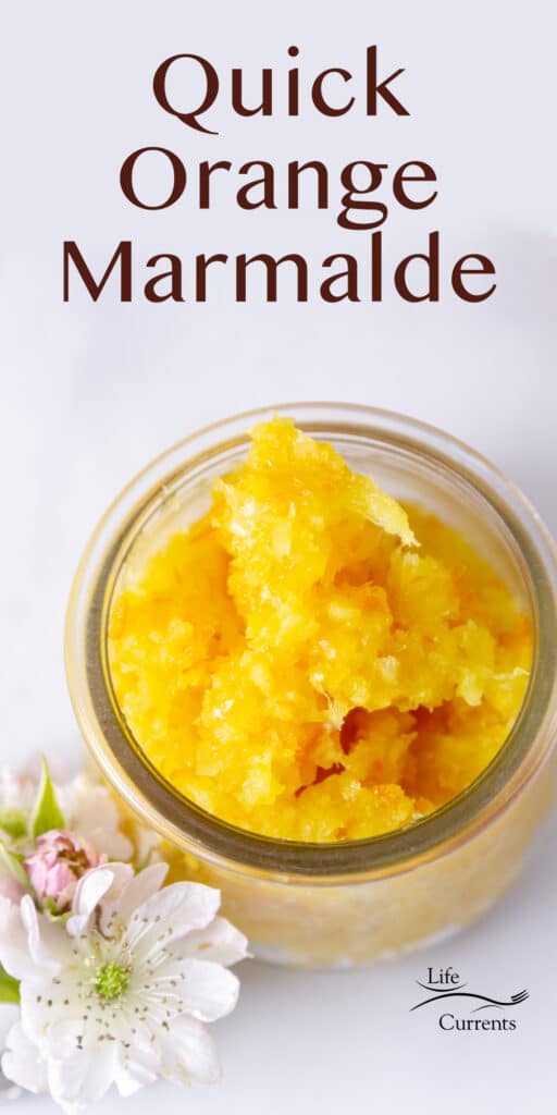 a glass jar filled with orange marmalade and some flowers next to it.