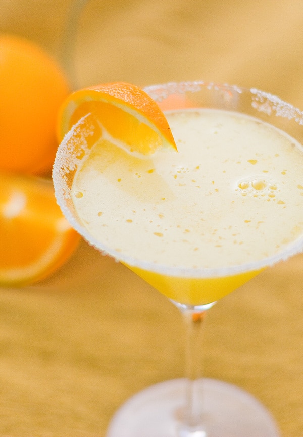 a martini glass with an orange slice on the side with oranges in the background.