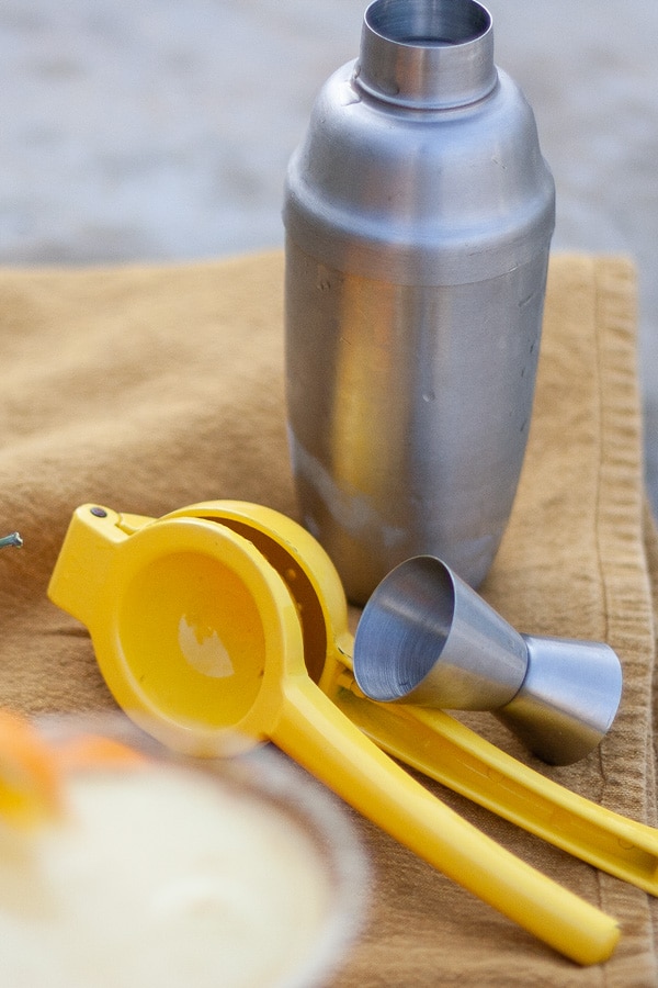 a cocktail shaker, measuring cup, and lemon squeezer.