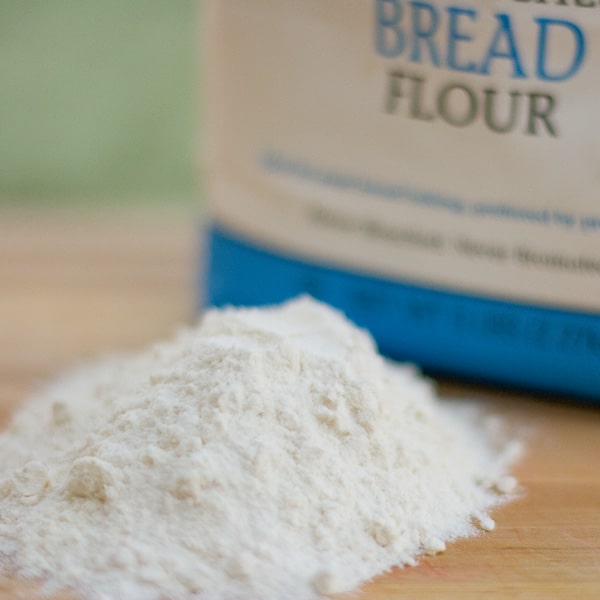 a pile of bread flour next to the bag on a wooden cutting board.