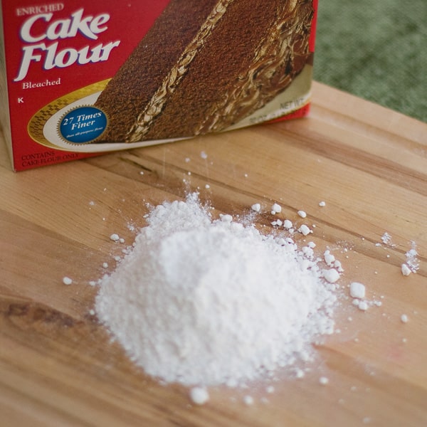 a wooden cutting board with a pile of cake flour on it and the box is next to the pile.