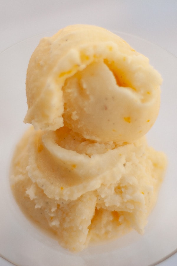 two scoops of sherbet in a glass bowl on a white background.