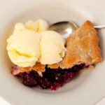 looking down on a slice of blackberry pie with buttermilk ice cream and a spoon.