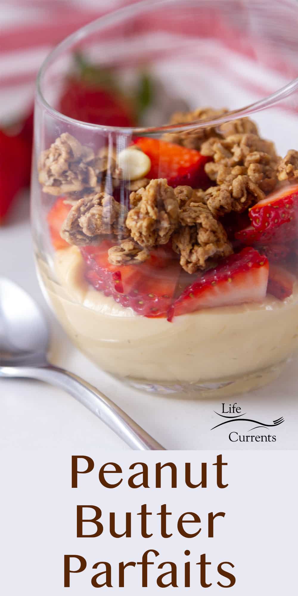 a parfait made with peanut butter, yogurt, granola, and fruit in a wine glass with a spoon in front of it.