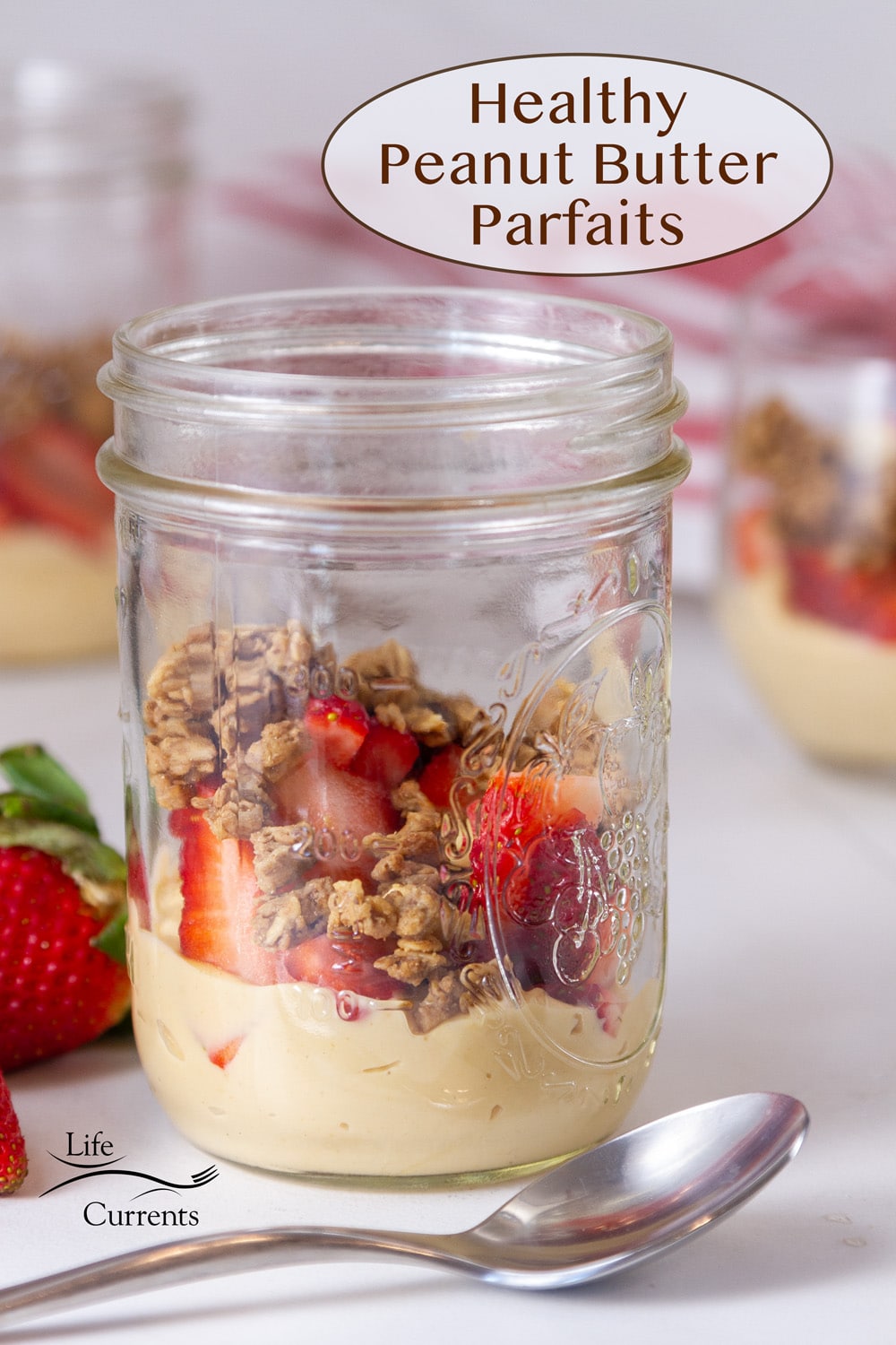 a mason jar filled with peanut butter, strawberries, and granola, a spoon in front of the jar.