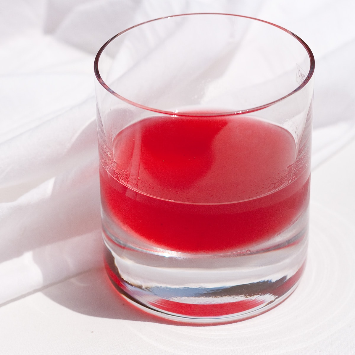 raspberry lime simple syrup in an old fashioned glass on a white background.