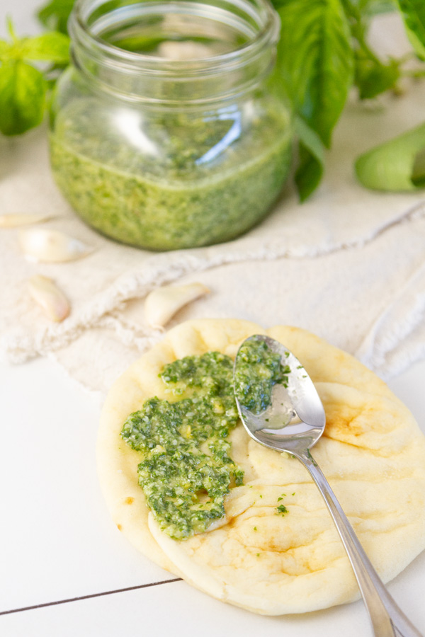 spreading basil pesto on a flatbread with a spoon.