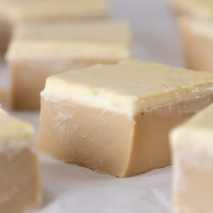 square crop of a coffee gelatin treat topped with cream layer cut into squares and placed on parchment paper.