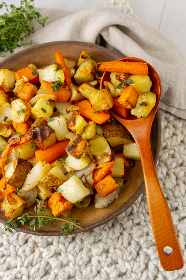 A bowl full of roasted root vegetables with a wooden serving spoon.