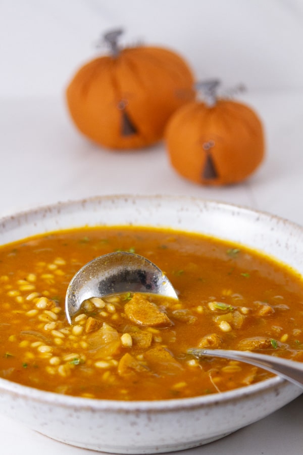 A big bowl of soup with a ladle in it in front of two jack-o-lanterns.