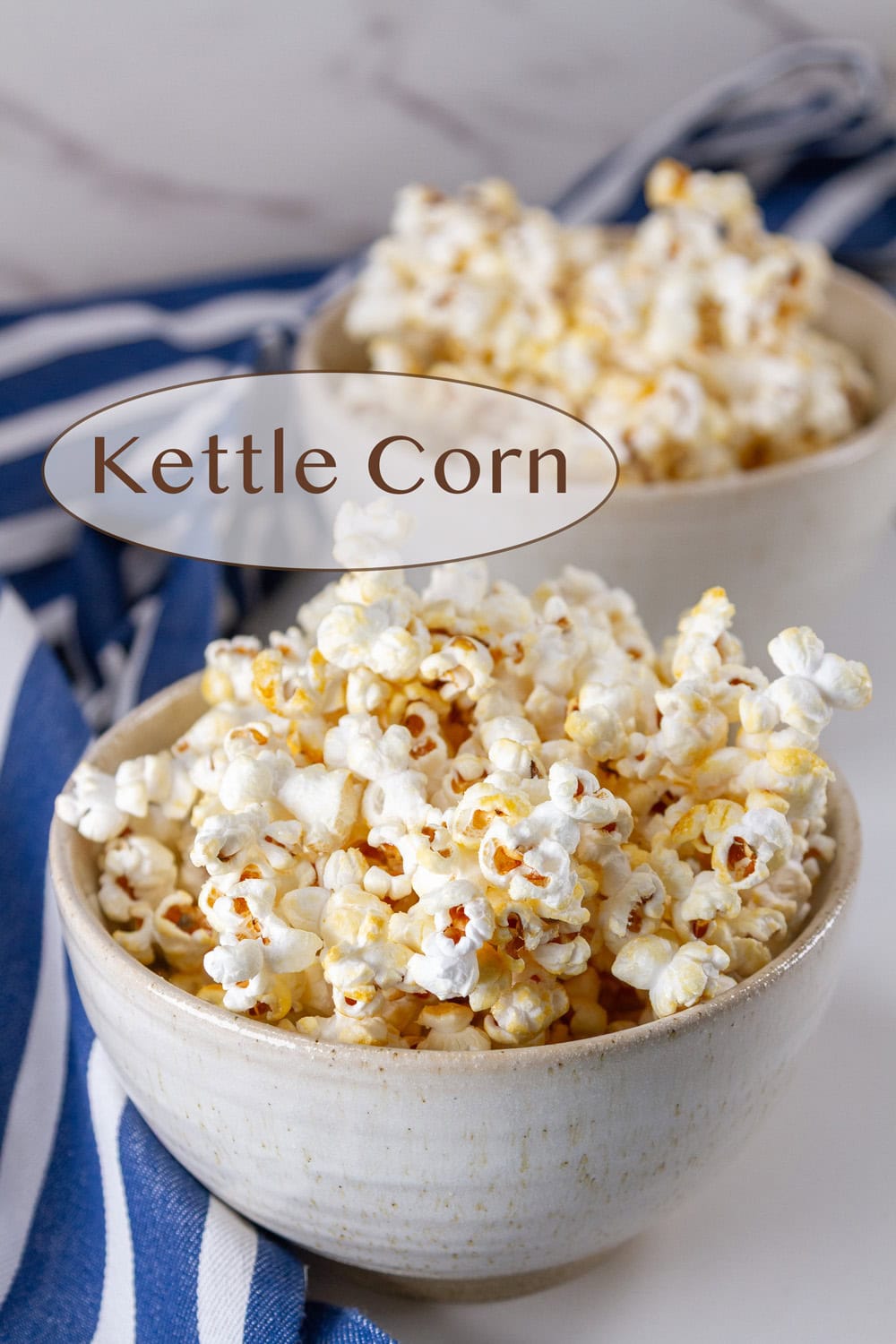 two white bowls filled with popcorn snack and a blue striped apron behind them.