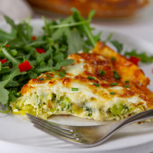 square crop of a slice of quiche on a plate with a salad.