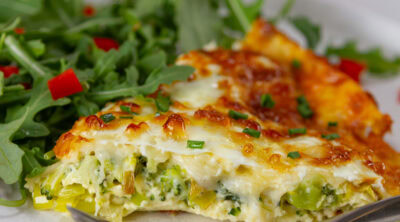 square crop of a slice of quiche on a plate with a salad.