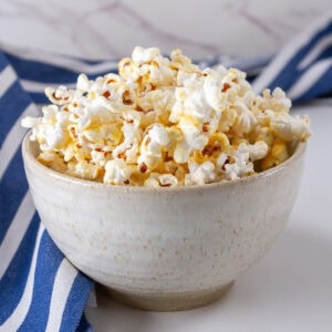 square crop of a bowl of kettle corn and a blue striped apron in the background.