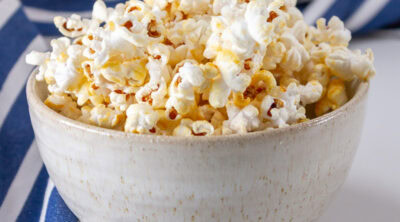 square crop of a bowl of kettle corn and a blue striped apron in the background.