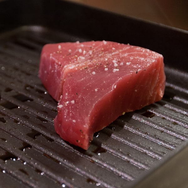 The two tuna steaks have been seasoned and placed in the hot grill pan - you can see the salt, pepper, and hot oil