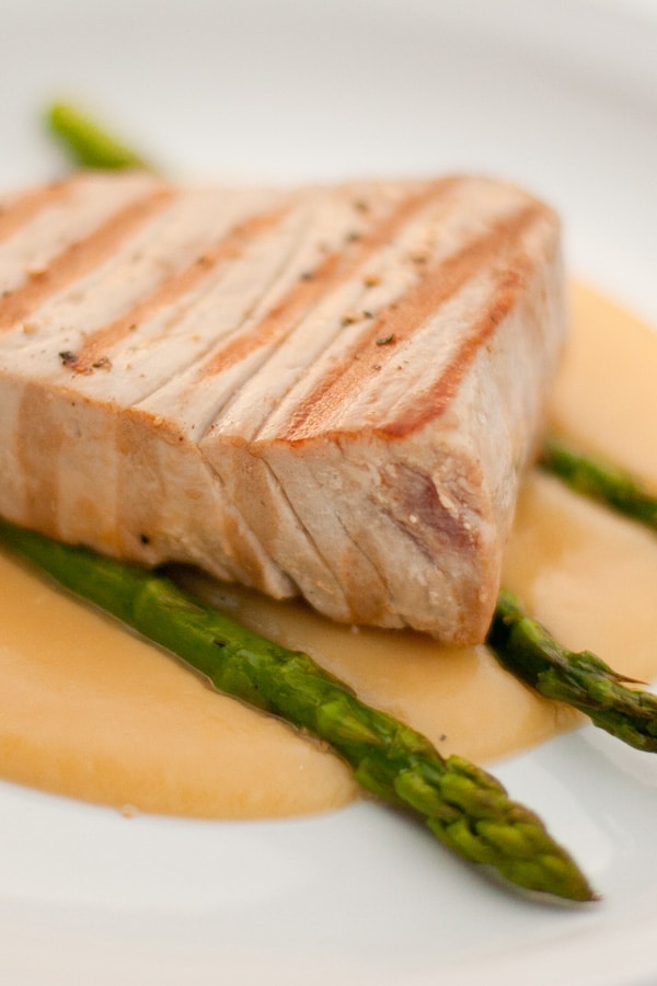 a whole piece of cooked tuna on top of asparagus and creamy sauce.