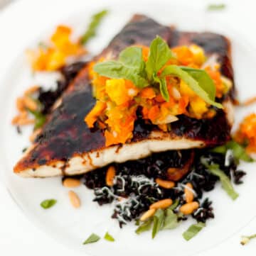 square crop of a piece of cooked fish with soy sauce glaze, pineapple salsa on top served on black rice.