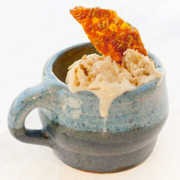 a blue mug filled with cice cream that's drizzled down the side and a candy shard.