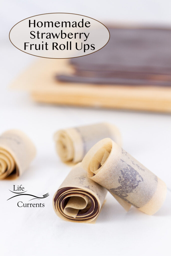 strawberry fruit roll ups in parchment paper in front of a cutting board with the rest of the fruit smash on it, title on upper left of image.