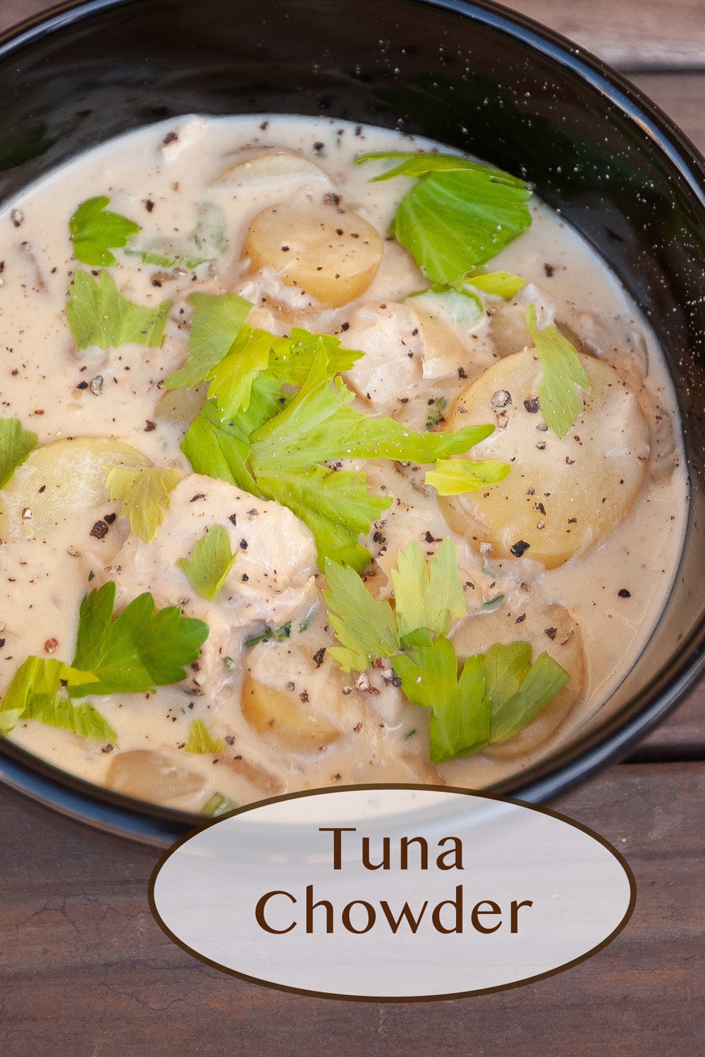 a black bowl filled with tuna chowder topped with celery leaves and pepper.