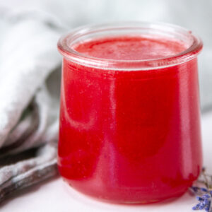 square crop of a glass jar filled with plum syrup in front of a green cloth napkin.