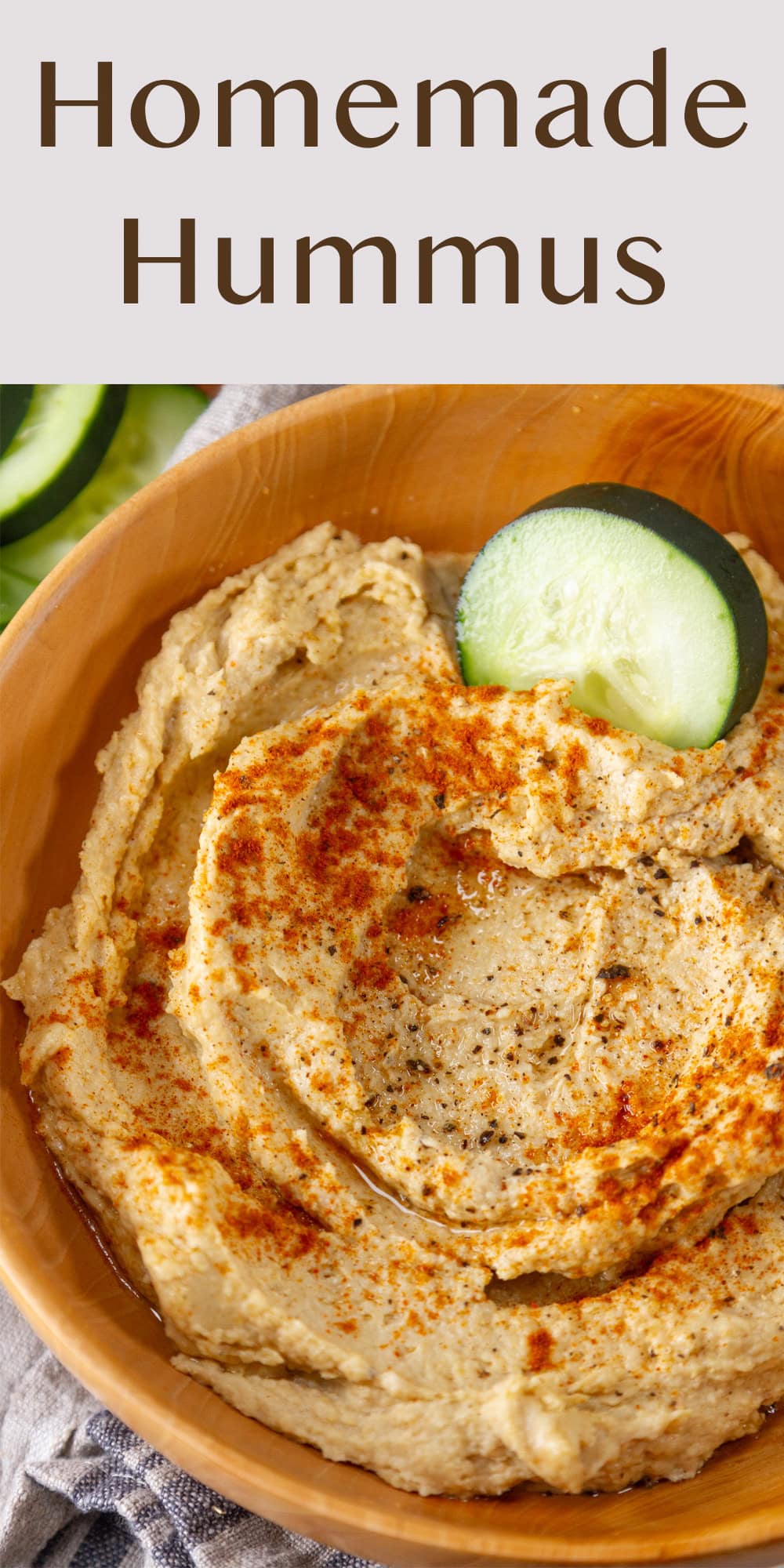 a wooden bowl filled with hummus and a cucumber slice is in the hummus.