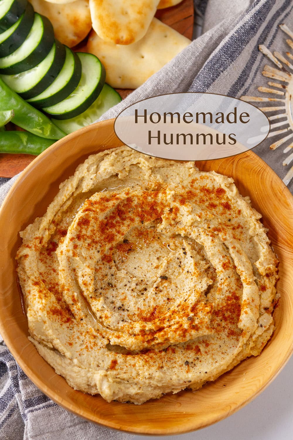 a wooden bowl filled with hummus and some veggies and naan next to the bowl.