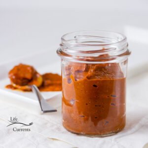 a jar filled with red paste in front of a spoonful of the paste