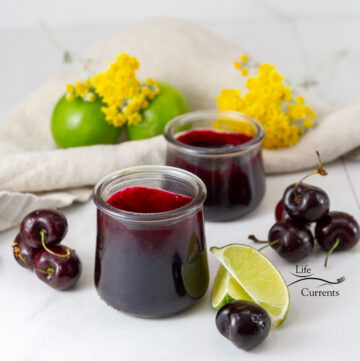 square crop of two jars of jam next to some cherries, limes, and yellow flowers.