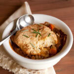 a white ramekin bowl with lentil pot pie with biscuit crust and a spoon in the dish.