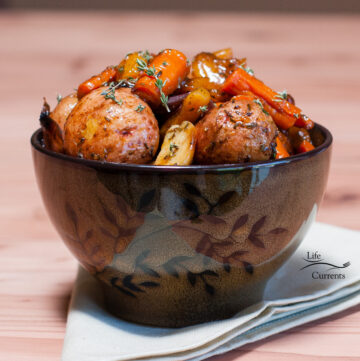 A dark colored bowl on a cloth napkin filled with veggies like potatoes and carrots