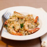 square crop of a bowl of rice, shrimp, and zucchini with a fork on the left side.
