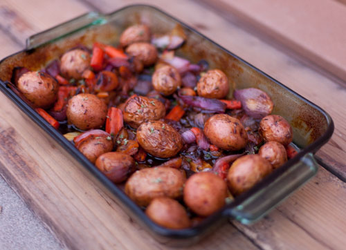 potatoes, carrots, red onions in a baking dish with herbs and sauce.