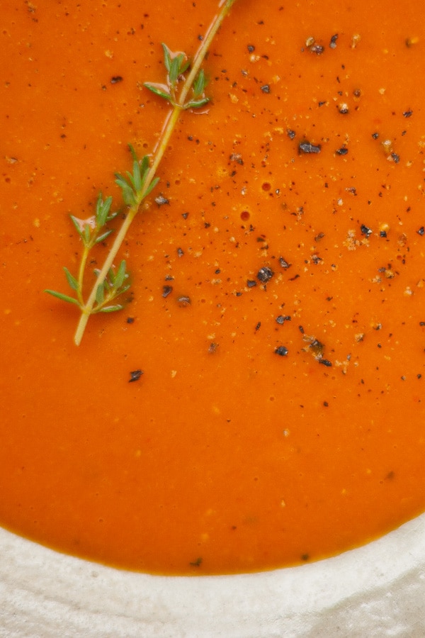 close up on red soup garnished with black pepper and a thyme spring.