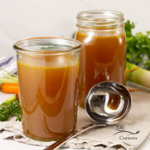 square crop of two jars of vegetable broth and a ladle next to them.