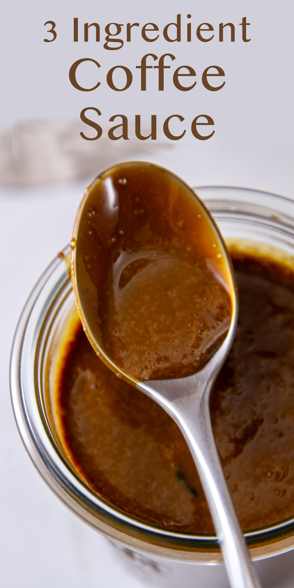 a spoon with dark brown dessert sauce in it on top of a jar of the sauce.