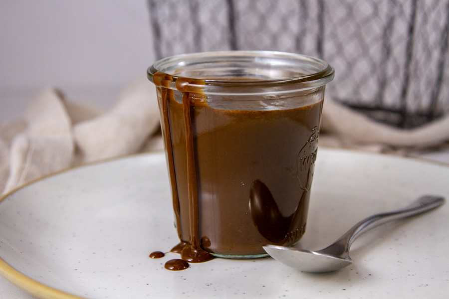 horizontal crop of a glass jar filled with sauce and a spoon to the right.