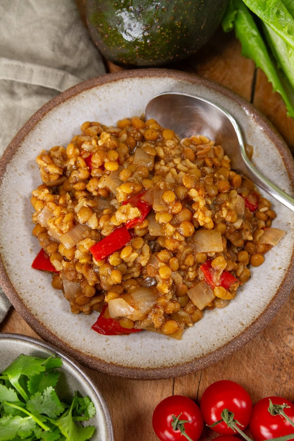 a plate for cooked lentils and rice with cilantro, tomatoes, and lettuce around it.