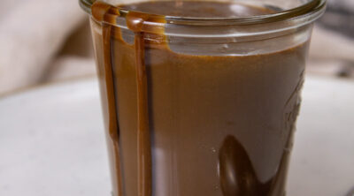 a glass jar filled with coffee sauce and some has spilled over the side, there's a spoon to the right.