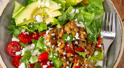 square crop of a bowl of salad with lentils, tomatoes, avocado, and chips, a fork on the right.