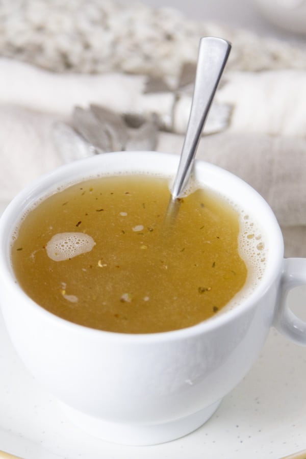 A white cup filled with vegetable broth made from Vegetable Broth Powder, a spoon in the cup.