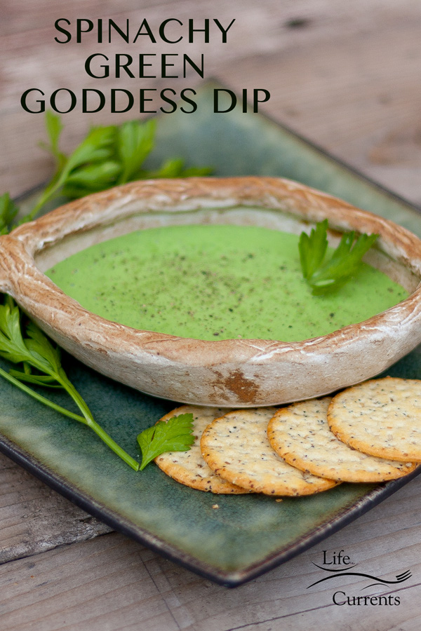 Green dressing in a brown bowl with crackers, cilantro, and pepper. On a green plate on a wood background